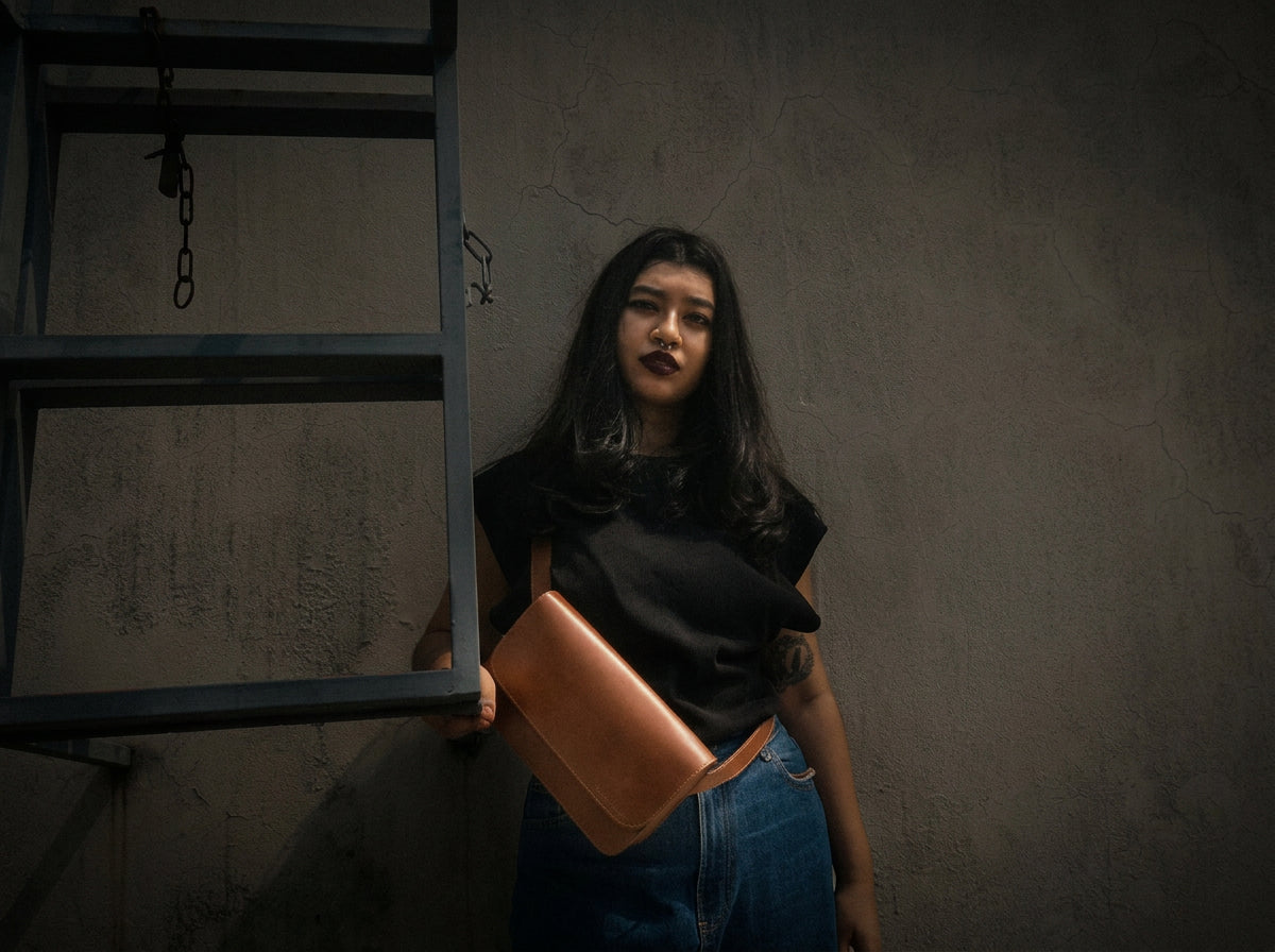Worn against a workshop wall in Dhaka — tan leather crossbody